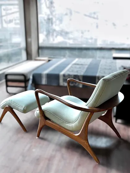 A different view of the curved teak lounge chair, showcasing the elegant form of its back and armrests. Placed in a room with large windows, it becomes an ideal spot for relaxation and enjoying the view.