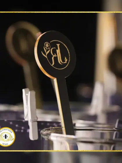 A close-up of a custom-designed drink stirrer. This elegant black and gold stirrer, featuring the couple's initials, elevates a simple glass into a personalized statement.