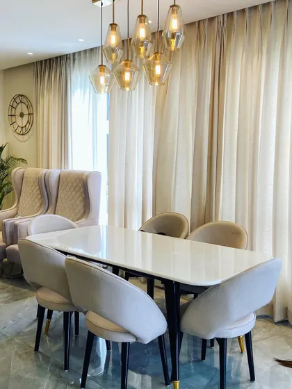 The dining area is positioned near a window, allowing for plenty of natural light during the day. The elegant wingback chairs in the background are part of the adjacent living area.