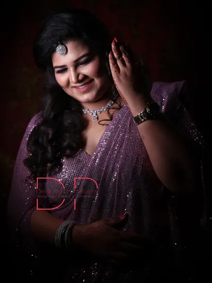 A studio-style portrait with dramatic lighting, highlighting the bride's sparkling purple saree, diamond jewelry, and gentle smile.