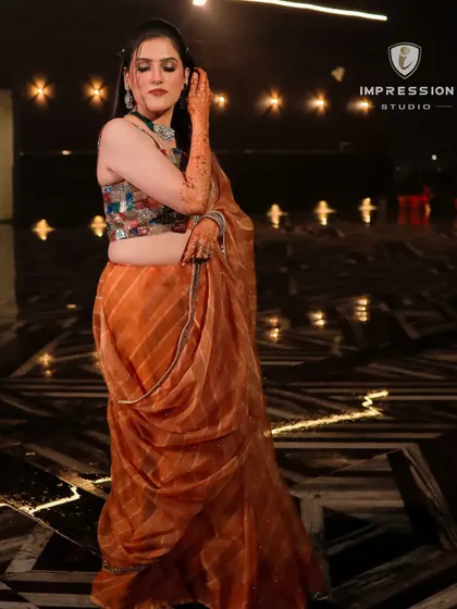 A full-length shot of the bride posing elegantly in her orange saree during her mehndi function at Winsome Resorts, Jim Corbett.
