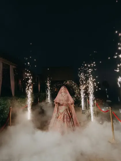 A powerful shot of Radhika's entrance, shrouded in smoke and flanked by pyrotechnics. This image captures the grandeur and excitement of a modern bridal entry.