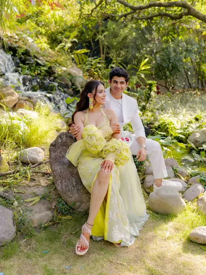 A lovely couple portrait from a Haldi or Mehendi event. The couple is dressed in coordinated yellow and white, sitting together in a beautiful garden setting.