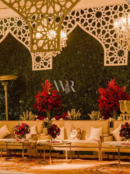 A closer view of the lounge under the jaali canopy. The back wall is a lush vertical garden, against which the vibrant red floral arrangements provide a stunning pop of color.
