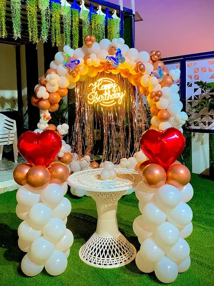 A beautiful outdoor birthday setup on an artificial lawn. The decor includes a balloon ring with a neon sign, heart-shaped foil balloons, and a small table, perfect for a romantic evening.