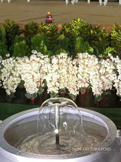 The soothing sound of water adds another sensory layer to the decor. This small fountain is surrounded by white blossoms, creating a tranquil and beautiful focal point in the garden.