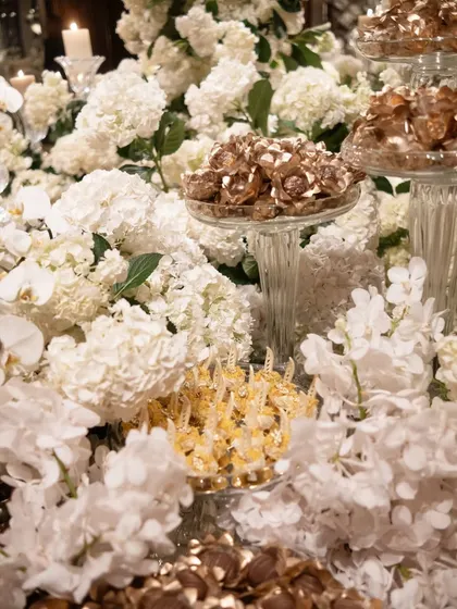 A dessert display where sweets and chocolates are nestled amongst clouds of white hydrangeas and orchids. This creative presentation makes the food a part of the decor.