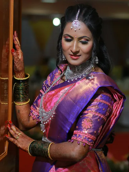 A classic portrait of a bride in a purple and pink silk saree, adorned with diamond jewelry.
