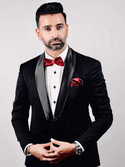 A portrait of our head designer in a classic black tuxedo with a satin shawl lapel and a striking red bow tie. This is a timeless look, executed with the precision of bespoke tailoring.