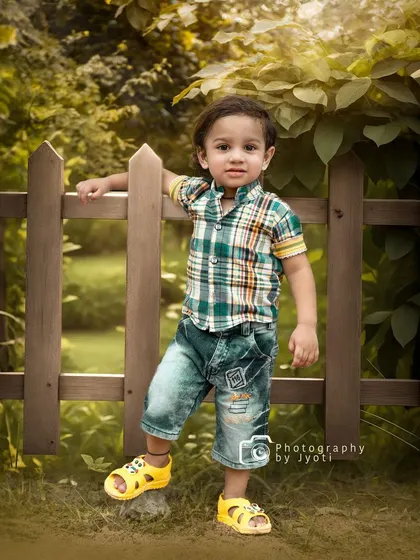 A confident pose from a little boy during his outdoor photoshoot, leaning against a wooden fence in a park. I aim to capture the unique personality of every child.