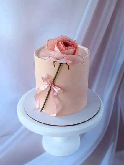 A minimalist pastel pink cake featuring a single, handcrafted wafer paper rose and a delicate ribbon. This design is all about simple elegance.