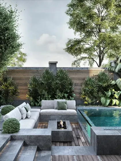 A luxurious poolside retreat designed for ultimate relaxation. This landscape plan features a modern fire pit, comfortable all-weather sofas, and lush, layered planting that provides privacy and a tropical feel. The combination of stone, wood, water, and fire creates a balanced and sophisticated outdoor lounge.