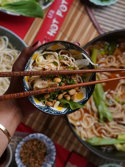 A close up shot of a hand holding a bowl filled with noodles and broth from the Hot Pot. This personal perspective makes you feel like you're right there, ready to take your first delicious bite.