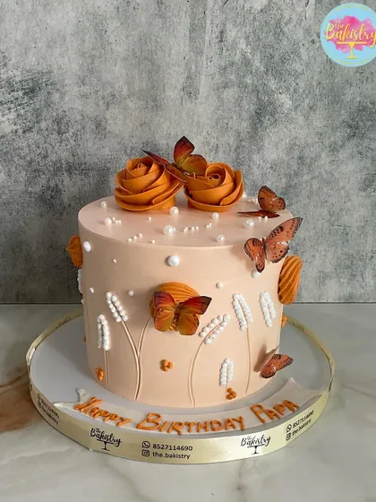 A beautiful peach-colored cake adorned with orange butterflies and roses for "Papa's" birthday.