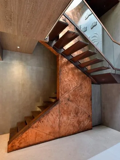 This sculptural staircase is a centerpiece, crafted from copper and metal with cantilevered wooden treads. It embodies a dialogue between lightness and intensity, transforming the act of ascent into a sensory experience, complemented by the natural light from a circular skylight above.