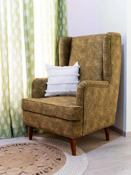 A quintessentially country-style wingback chair, custom-upholstered in a textured olive fabric. Placed in a cozy corner with a jute rug, it creates the perfect reading nook or a comfortable spot for quiet contemplation.