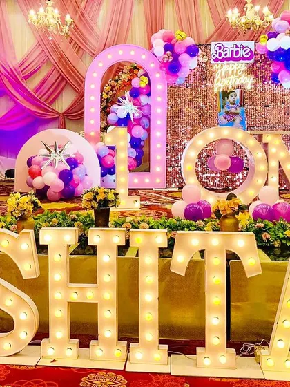 A glamorous Barbie-themed first birthday party. The stage is filled with pink decor, a sequin wall, and large marquee letters for the name and the word "ONE".