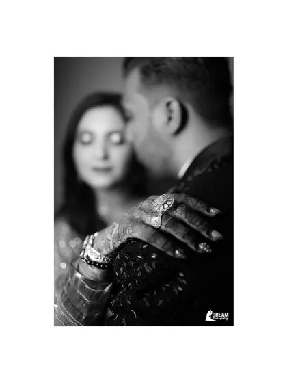A close-up black and white shot focusing on Ekta's hand, adorned with her engagement ring, resting on Ashutosh's shoulder.