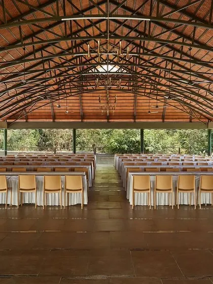 The interior of the main hall at Samavana, with its exposed steel truss roof and terracotta tiles. This large, column-free space offers maximum flexibility for event layouts, from wedding ceremonies to large dining setups.