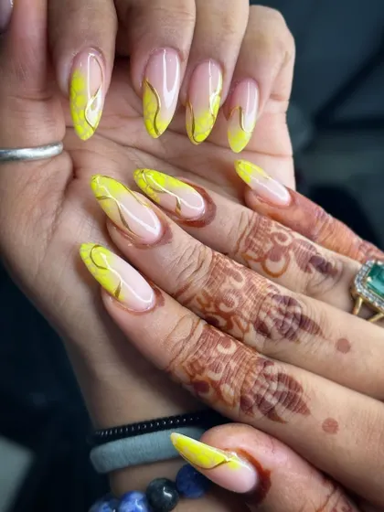 A bright and cheerful design featuring a vibrant yellow base with delicate gold chrome swirls. This look, paired with the client's mehndi, is perfect for festive occasions like Haldi ceremonies.