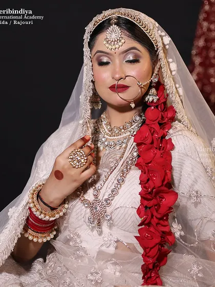An ethereal bridal look in a white lehenga, featuring a long, decorative braid adorned with red rose petals for a pop of color.