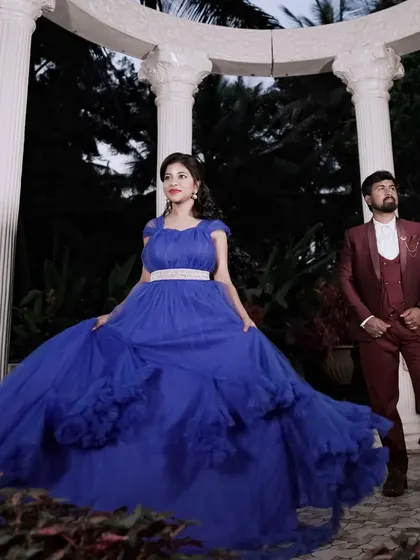 A grand and dramatic pre-wedding photo. The royal blue ball gown and the partner's maroon suit create a regal and sophisticated look, perfect for a palace-themed shoot.