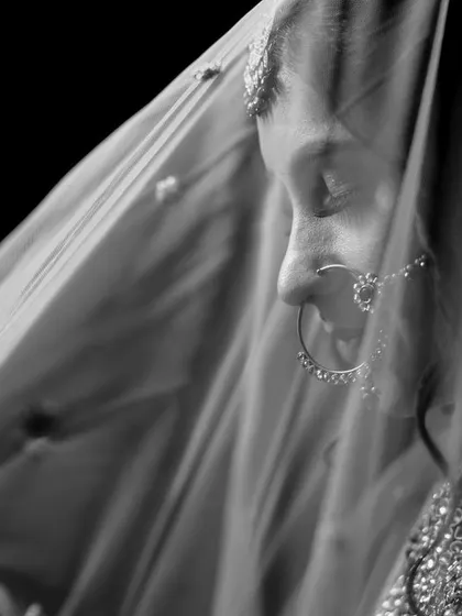 A classic black and white bridal portrait under the veil. The soft, diffused light creates a timeless and graceful image, highlighting her traditional nose ring.