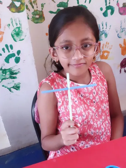 A young girl proudly holds up the straw helicopter she created, a simple yet effective demonstration of physics.