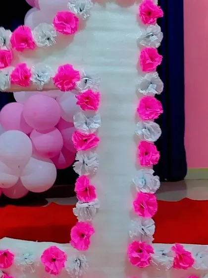 A large number '1' prop decorated with pink and white paper flowers, perfect for a first birthday.
