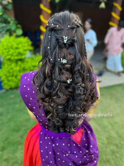 A bohemian-inspired half-up style with multiple braids and twists, accented with small floral clips. This textured look is perfect for a mehendi or a destination wedding.