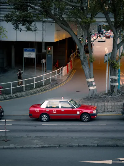 A side profile of the iconic red taxi, showing its distinct design against the urban backdrop. I took a series of photos to document this symbol of Hong Kong from various angles.