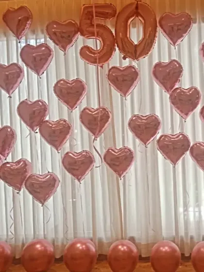 A full wall decoration for a 50th anniversary or birthday, featuring rose gold number balloons surrounded by a cascade of matching heart shaped foil balloons.