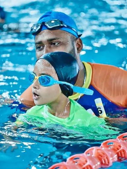 A coach guides a young swimmer, providing support and encouragement. Our Michael Phelps program focuses on building skills and confidence in a safe environment.