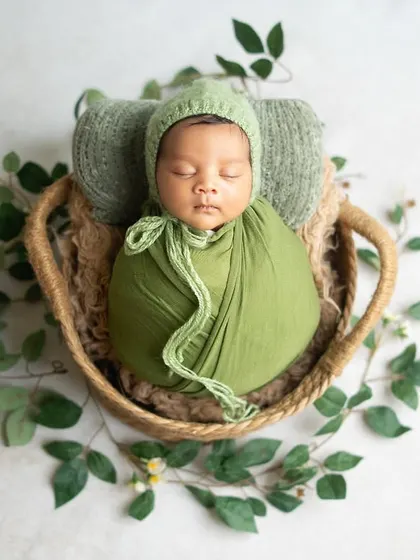 A newborn boy nestled in a basket with lush green wraps and ivy. This nature-inspired setup is perfect for creating a calm and organic feel.