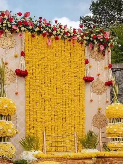 An elegant Haldi seating backdrop made of marigold strings and accented with red and white flowers.