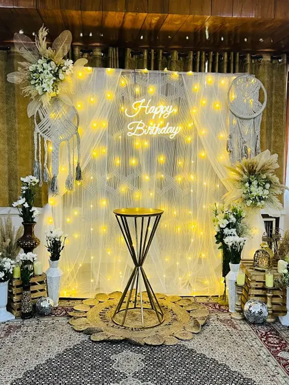 Even small spaces can be transformed for an intimate and stylish birthday. This cozy at-home boho decoration features a fairy light curtain, macrame dreamcatchers, and pampas grass for a warm and picture-perfect celebration.