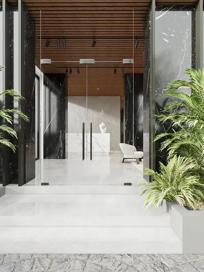 The entrance to this lobby is designed like a story, with a clear focal point. The bold black marble pillars frame the view into the bright, welcoming space, while lush planters soften the modern architecture.