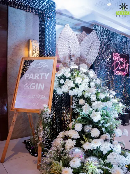 Setting the party mood right from the entrance. This welcome setup for a cocktail night features a shimmering sequin wall, lush white flowers, and a fun neon sign to get the celebration started.