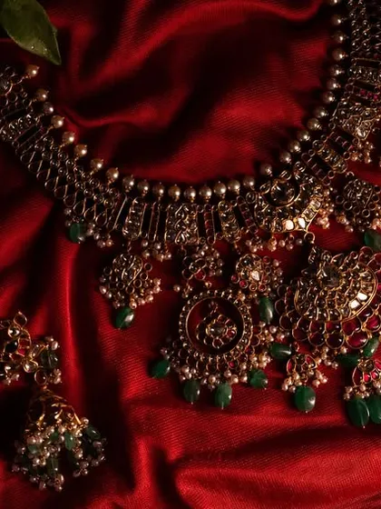 A close-up of an exquisite antique-finish temple jewelry set, with intricate details and green stones, resting on a rich red silk cloth.