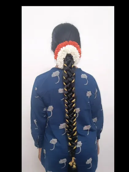 A very long, neat fishtail braid with a gold ribbon criss-cross pattern, finished with a tricolor floral arrangement.