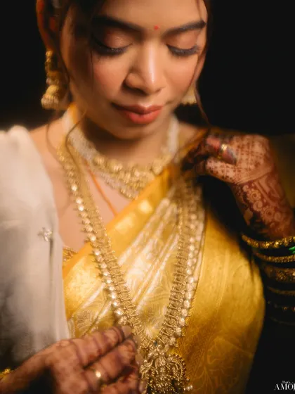 A stunning low-light portrait of the bride. The soft, dramatic lighting highlights her features and the intricate details of her gold jewelry against the dark background.