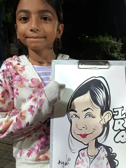 A young girl with a shy smile holding her caricature. I always aim to create a drawing that is fun but also a good likeness.