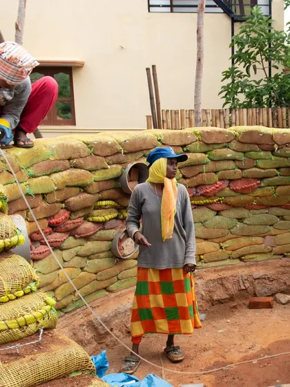 Women constructing a curved earthbag wall, a technique that allows for creative and organic forms in building. The colorful bags are made from upcycled onion sacks.