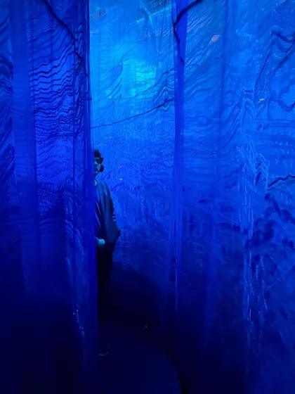 A visitor walks through the narrow passages of the 'Into The Deep' installation. The immersive blue light and textured fabric walls create a feeling of being submerged in an abstract, poetic ocean.