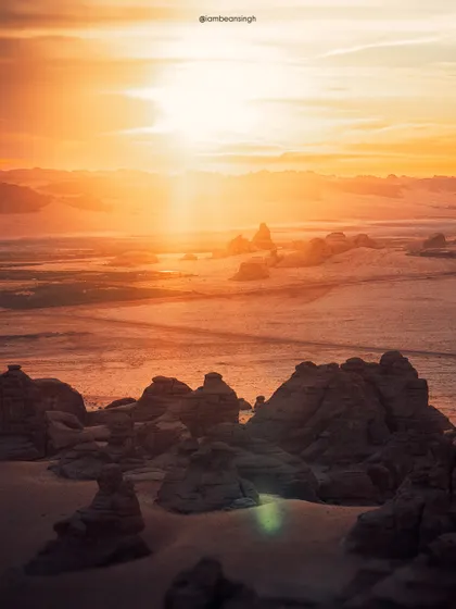 The golden light of sunrise washes over the rock formations of Hegra, Saudi Arabia. This landscape shot, taken from a hot air balloon, captures the epic scale and ancient beauty of the UNESCO World Heritage site.