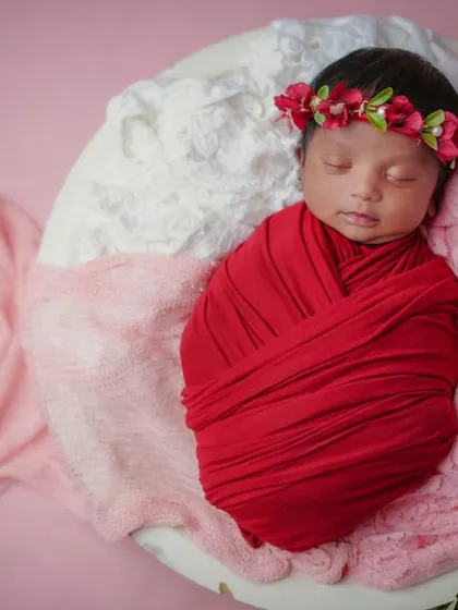 A little rosebud. Swaddled in red and wearing a floral crown, this baby is the picture of newborn beauty.