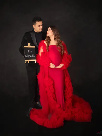A sweet gender reveal for a baby girl. The dad-to-be holds a small chalkboard sign while his partner glows in a beautiful red gown.