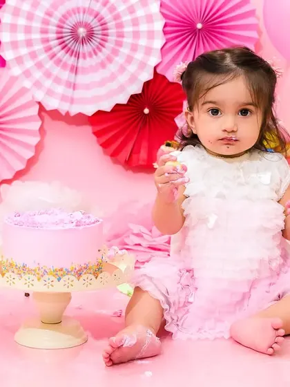 A baby girl delicately tastes the frosting from her cake during her pink-themed first birthday party.