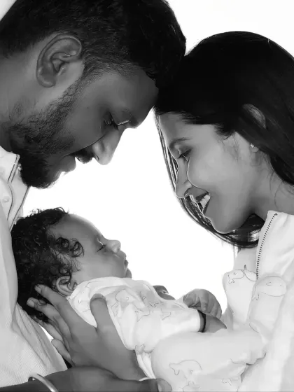 A beautiful black and white portrait of new parents gazing lovingly at their sleeping newborn.