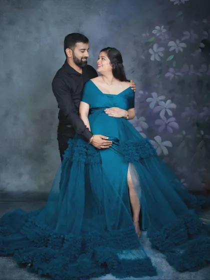 A beautiful couple's maternity photo, with the mother-to-be wearing an elegant teal gown with a ruffled train.